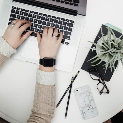 Manos de una mujer trabajando y escribiendo en una MacBook.